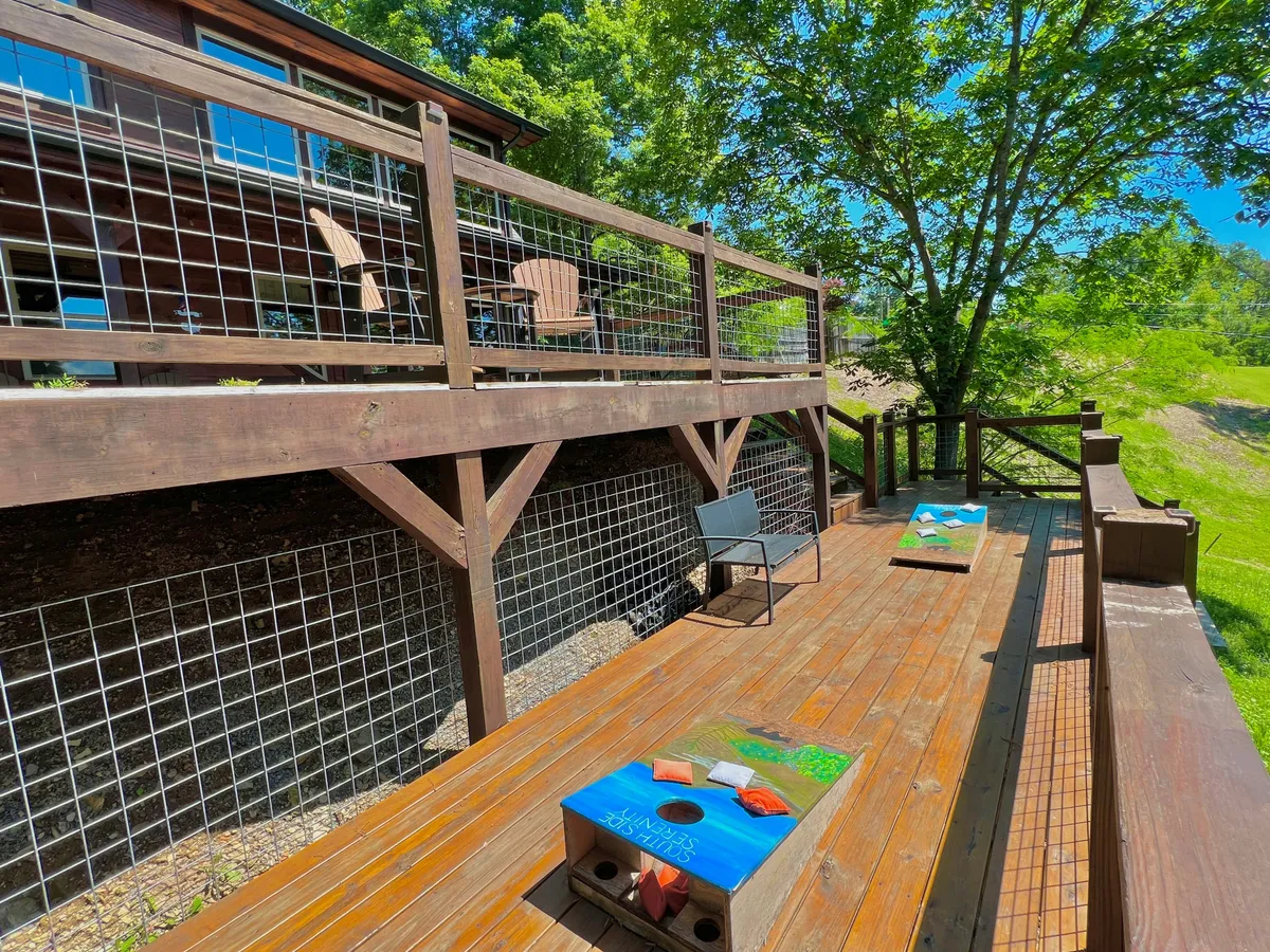 This cheerful scene features a wooden deck with patio chairs and cornhole boards, surrounded by tree foliage. The setup is casual and inviting, suggesting a lively space for games, laughter, and relaxation.