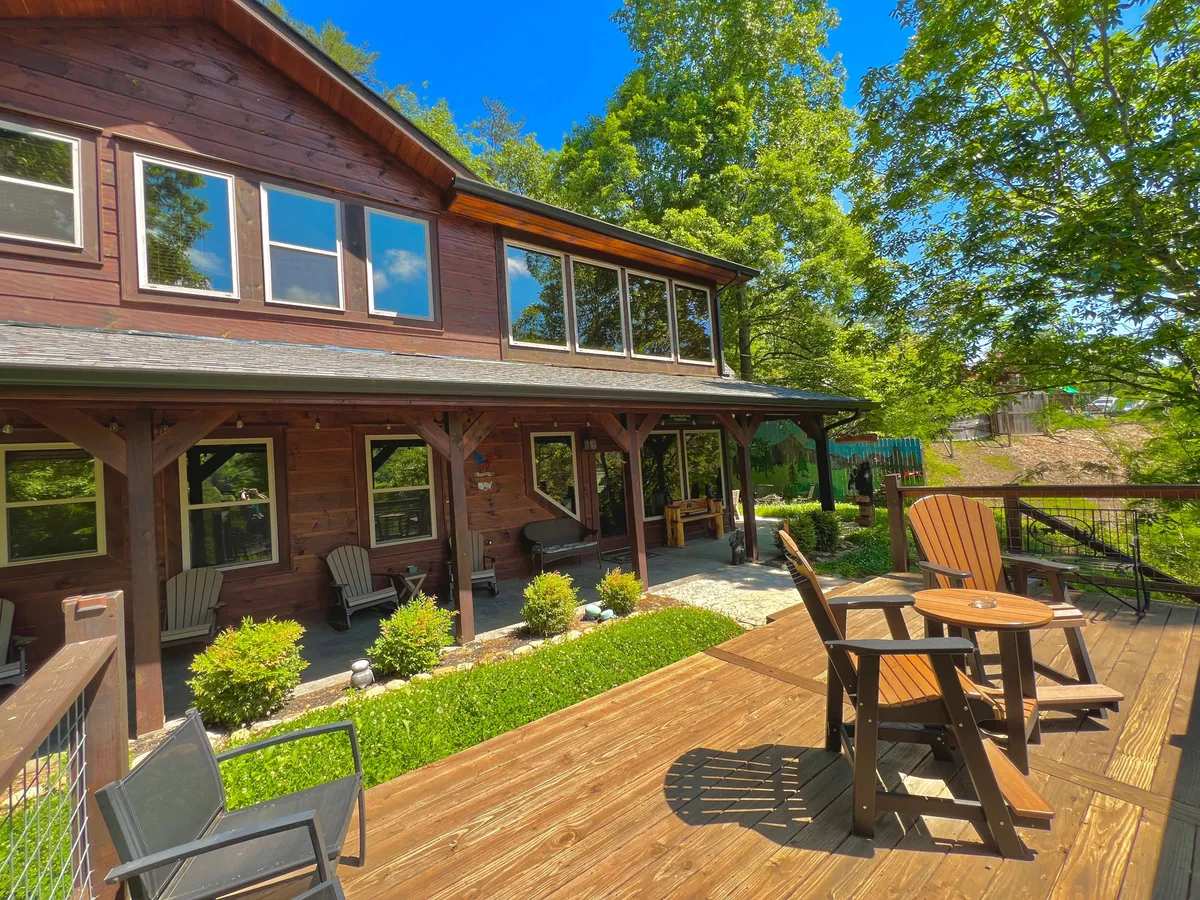 A wooden deck outside large windows, furnished with comfortable seating and surrounded by lush greenery. The space invites relaxation and easy access between indoors and outdoors, with a view perfect for enjoying fresh mountain air.
