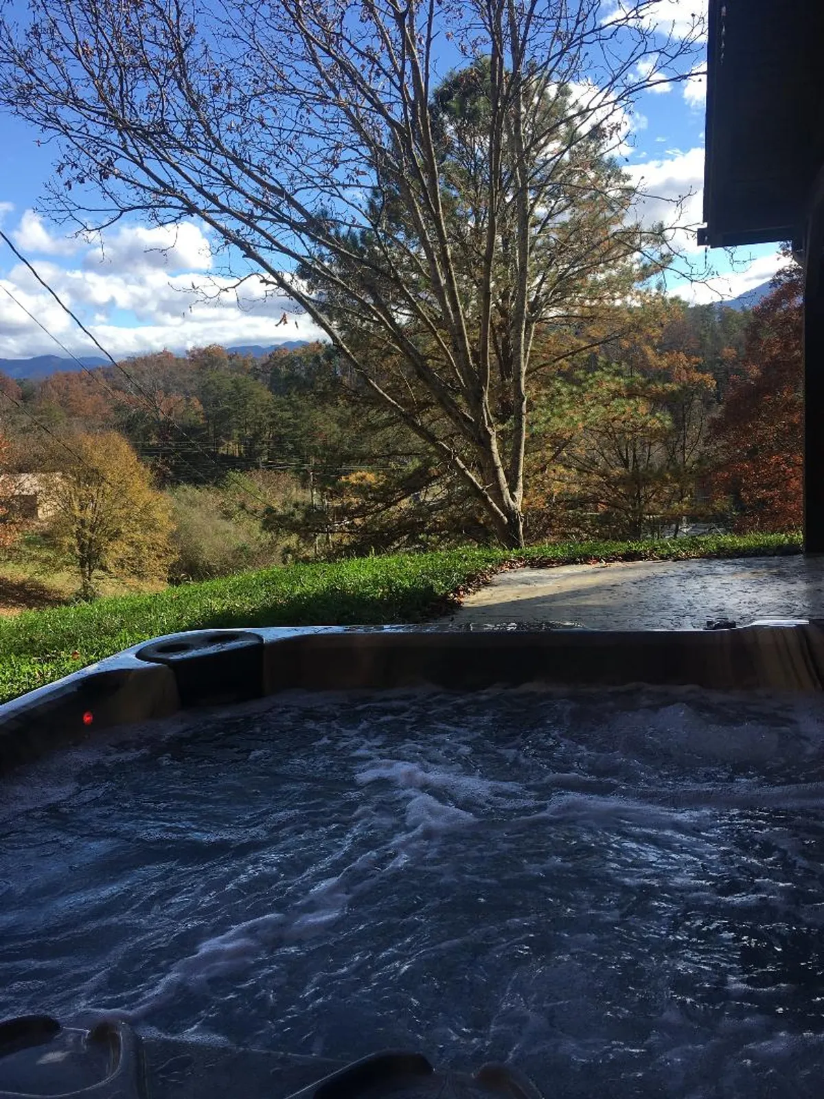 A tranquil outdoor scene featuring a hot tub set against a backdrop of scenic mountain views, surrounded by trees and open sky. The atmosphere is peaceful and conducive to relaxation or stargazing.