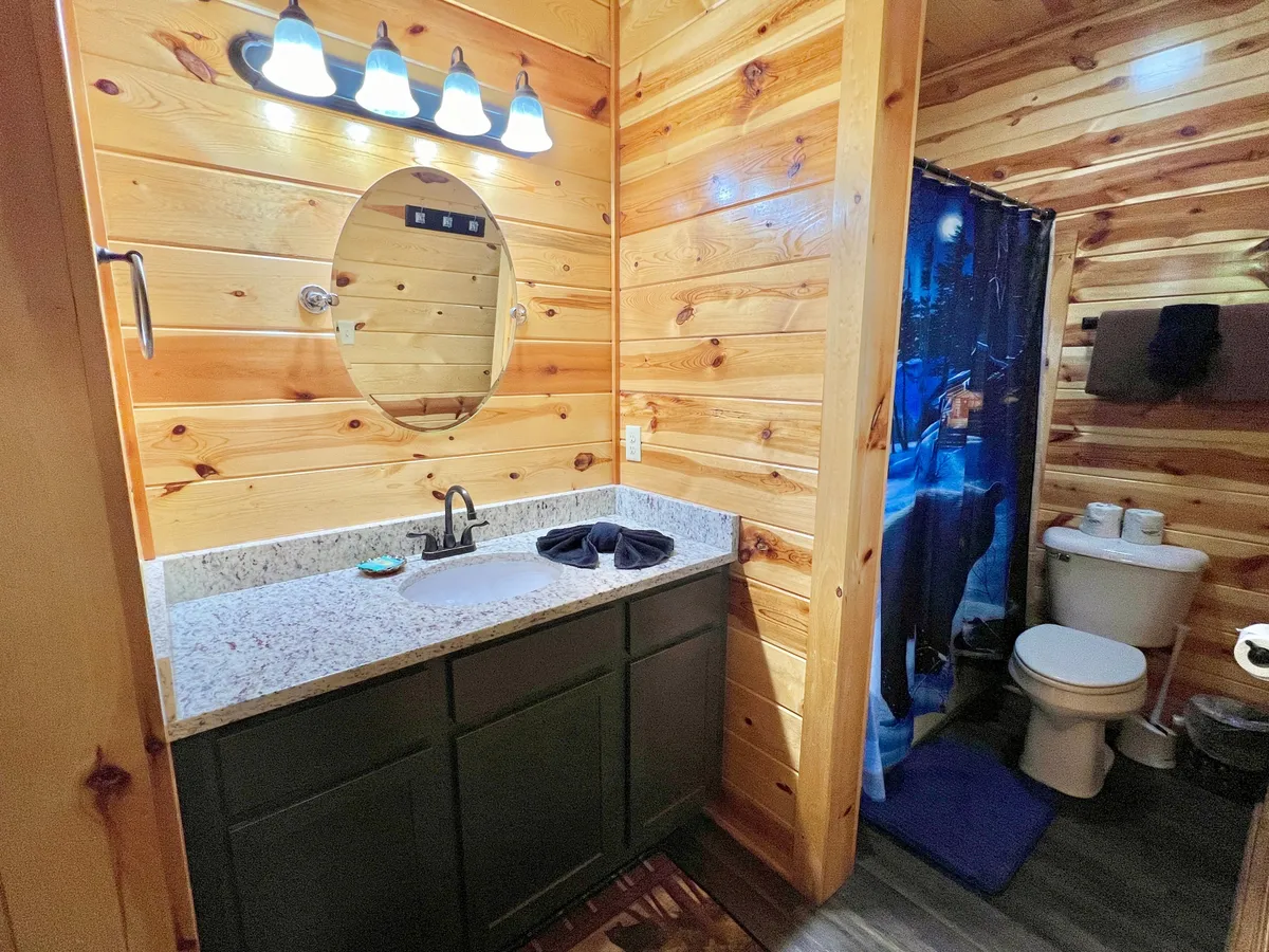 An inviting bathroom with a granite countertop, a mirror, wooden walls, and a shower curtain. The mood is warm and intimate, perfect for personal grooming or a refreshing shower after a day of mountain adventures.