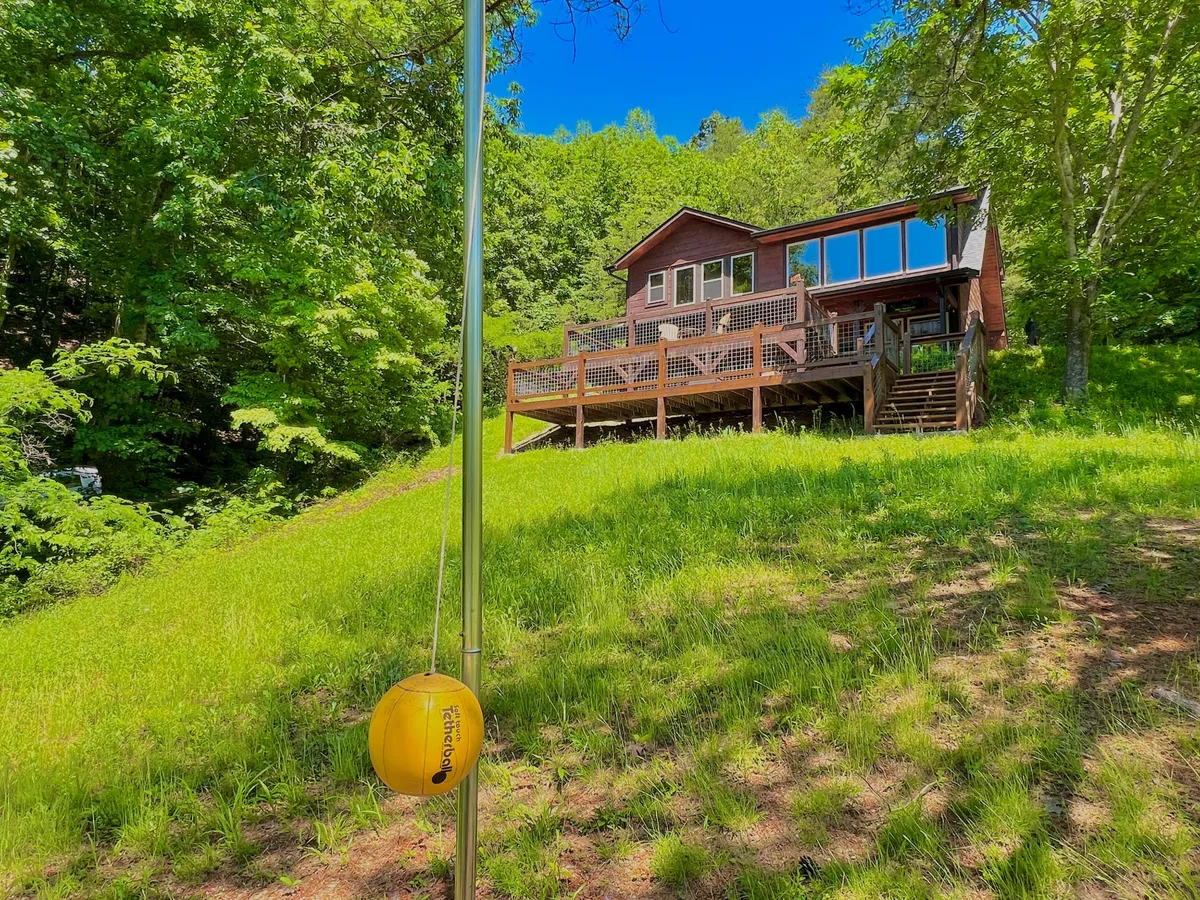 This photo shows the house's expansive deck with plenty of room for outdoor activities, a lush green lawn ideal for play, and large windows looking into the home—showcasing the effortless flow between indoor and outdoor spaces.