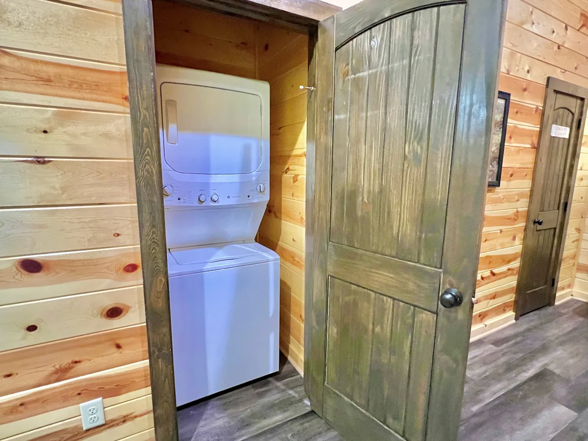 A practical view of the loft's stacked washer and dryer unit, set against textured wooden walls and a sturdy wooden door. The setup is neat and easily accessible, embodying the convenience of in-loft laundry for carefree family living.