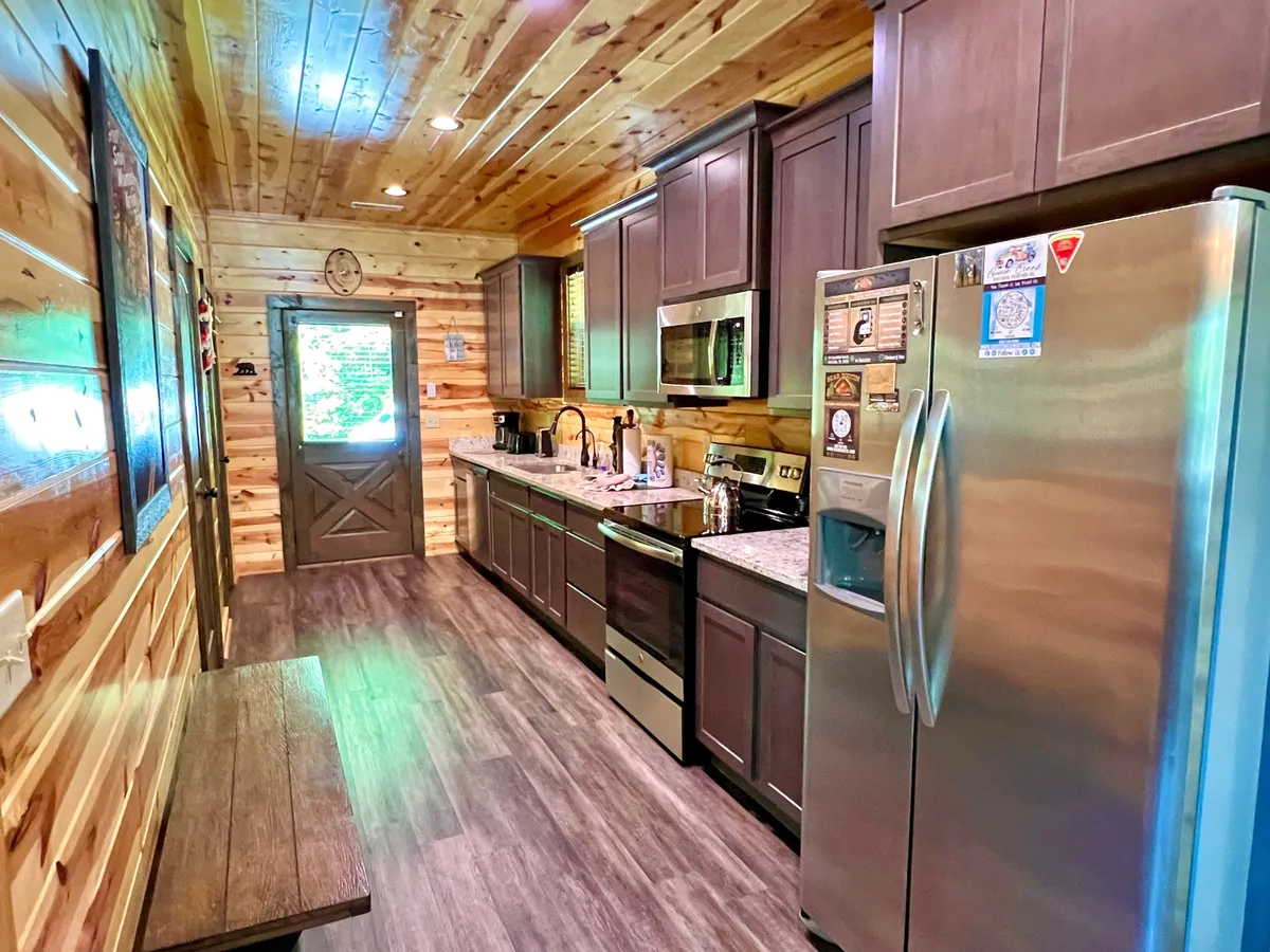 This image features a welcoming kitchen space with stainless steel appliances, granite countertops, and ample wooden cabinetry. A door leads outside, and the space is bathed in natural light, creating an inviting atmosphere for cooking or gathering.