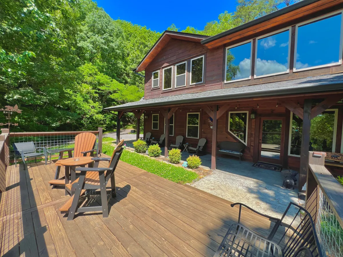 This image captures a spacious wooden deck with comfortable seating, surrounded by lush greenery and large windows that offer a glimpse of the inviting interior. The deck provides a tranquil setting for groups to gather, relax, and enjoy the beauty of nature together.